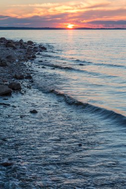 Dalgalar nehir, kayalık kıyısında yaz günbatımı çalıştırın.