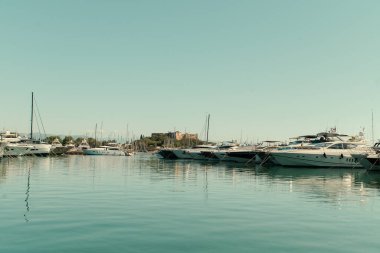 Sakin ve güneşli bir günde modern bir marinada demirlemiş lüks yatlar ve yelkenliler. Berrak su, seyahat ve yaşam tarzı üzerine yansımaları olan zarif bir kıyı şeridi..