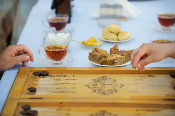 People play at the table with food, a board game backgammon Stock Image