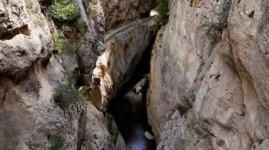 Engebeli ve sınırlı bir kanyon geçidinde süzülürken panoramik hava perspektifi. Dağın aşağısındaki akarsu, her iki taraftaki yüksek kayalıklarla çevrili, üsten geçiyor.