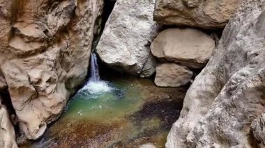Sert kaya oluşumlarıyla çevrili doğal bir turkuaz havuza akan gizli bir tatlı su çağlayanın yüksek açılı görüntüsü.