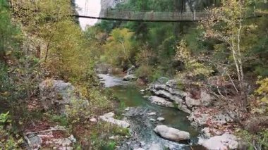 Kristal gibi berrak bir nehrin üzerinde geri geri uçarken manzara, çam ormanlarıyla çevrili, asma bir köprüyle dar bir kanyon geçidini açmak için açılıyor.