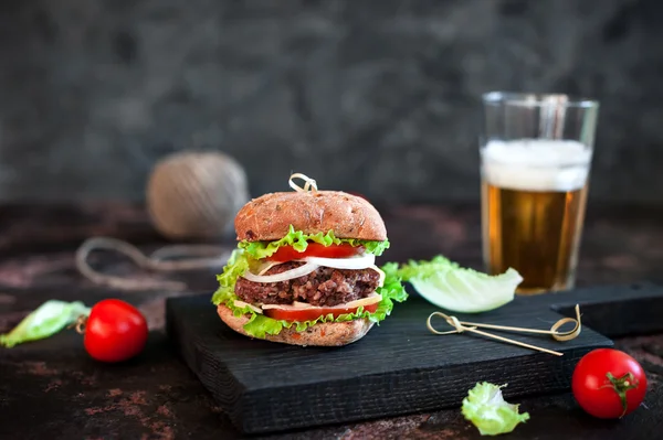 Grande hambúrguer saboroso com caneca de vidro de cerveja leve no fundo de madeira escura — Fotografia de Stock