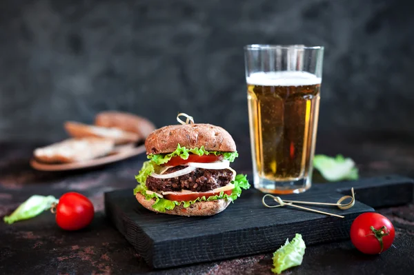 Grande gustoso hamburger con tazza di vetro di birra leggera su sfondo di legno scuro — Foto Stock