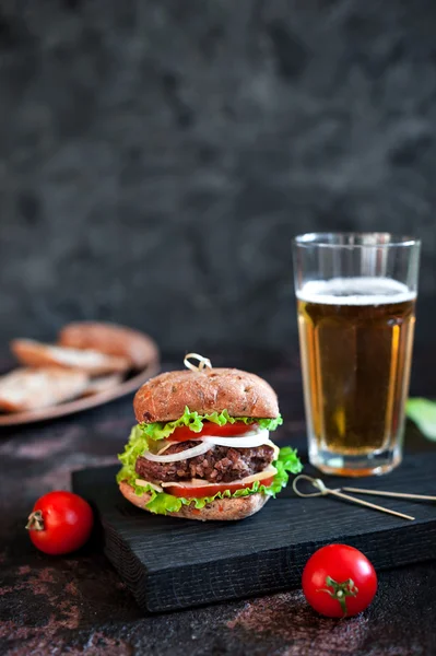 Grande hambúrguer saboroso com caneca de vidro de cerveja leve no fundo de madeira escura — Fotografia de Stock