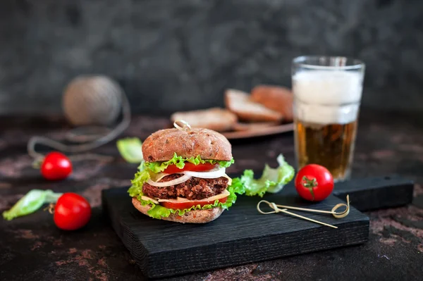 Grande hambúrguer saboroso com caneca de vidro de cerveja leve no fundo de madeira escura — Fotografia de Stock