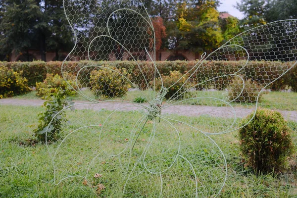 Bir tel örgü kelebek heykeli çalıların yakınındaki bir çimenlikte durur..