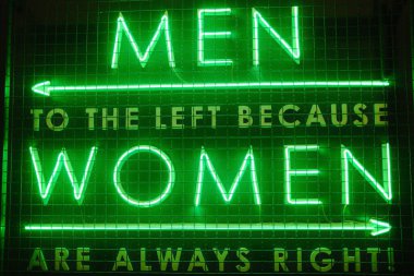 Bright green neon lettering shows a directional message regarding gender.