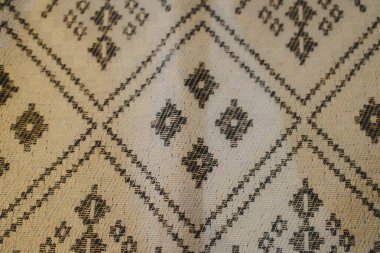 Dokuma kumaş, bej renginde karmaşık geometrik ve elmas desenlere sahiptir..