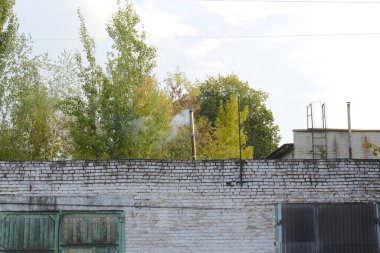 Tuğla bina garaj kapıları ve ağaçları gösteriyor. Duman bacadan geliyor..