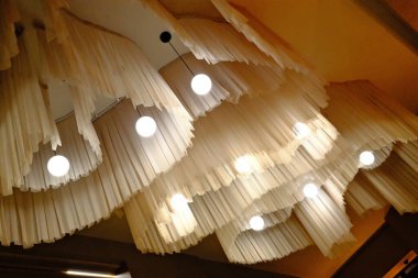 Krem kumaş katmanları tavandan süzülüyor, parlak küresel kolye ışıkları ile aydınlatılıyor dekoratif tasarımı aydınlatıyor..