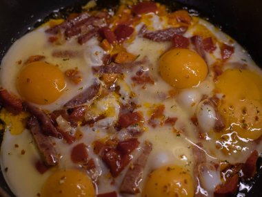 Close-up of scrambled eggs cooked with fresh vegetables and sliced sausage in a frying pan. Delicious homemade breakfast.