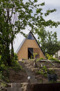 Ön planda yakacak odunları olan, ön planda çakıl yolu ve merdivenleri olan metal bir ızgaranın dikey aşağı fotoğrafı. Arka planda, yabani otlar.