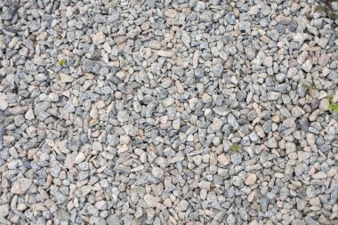 Üzerinde ara sıra yeşil bitkilerin filizlendiği kaba bir çakıl yolunun yatay tepeden aşağı fotoğrafı. Arkaplan olarak nötr, doğal doku ideali