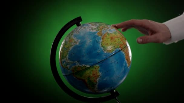 Mans hand rotates globe on green background — Stock Video