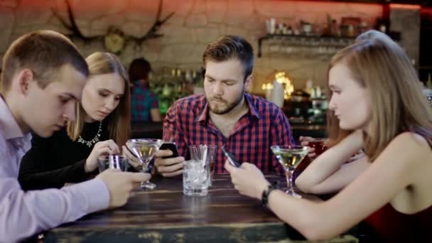 Společnost mladých lidí se dívá na jejich mobilní telefony v baru — Stock video