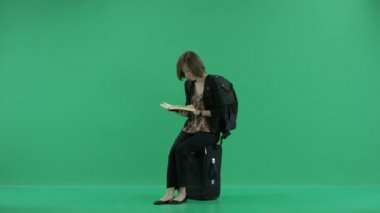 kadın turist okur ve bavul üzerinde oturan telefonda konuşuyor