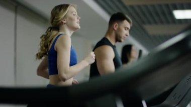 Çok gülümseyen sarışın kadın koşu bandı üzerinde çalışan