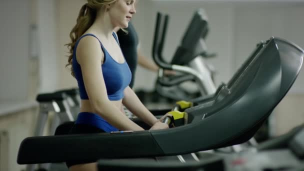 Mujer rubia bastante sonriente caminando en la cinta de correr — Vídeos de Stock