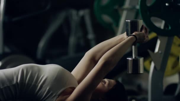 Mujer haciendo un ejercicio de jersey de mancuerna en un banco en un gimnasio . — Vídeo de stock