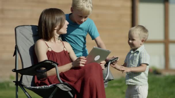 Niños mirando una tableta con su madre en un parque — Vídeos de Stock