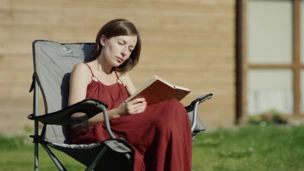 Joven mujer atractiva leyendo libro junto al árbol en el parque, dolly shot — Vídeos de Stock