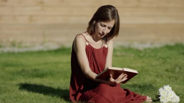 Jovem mulher atraente leitura livro pela árvore no parque, dolly shot — Vídeo de Stock