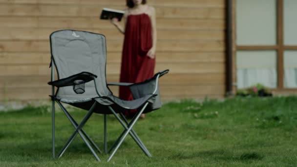 Молодая привлекательная женщина читает книгу у дерева в парке, снимает тележку — стоковое видео