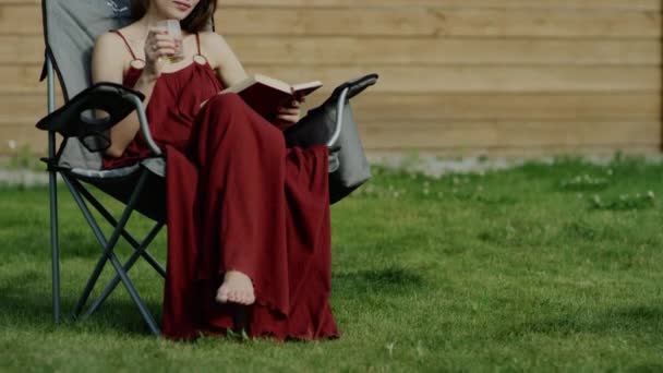 Jovem mulher atraente leitura livro pela árvore no parque, dolly shot — Vídeo de Stock