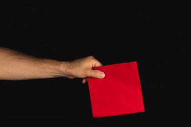 Parlak kırmızı bir zarfı kavrayan bir el, koyu arkaplan ile çarpıcı bir kontrast oluşturur. Sahne zarfın canlı rengi ve dokusuna odaklanıyor..