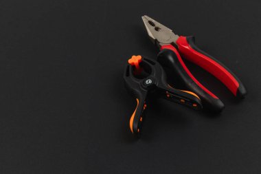 Bir çift alet kullanılmaya hazır karanlık bir yüzeyde duruyor. Pense ve klemp vitrin canlı renkleri göze çarpıyor, ev geliştirme görevleri için ideal.