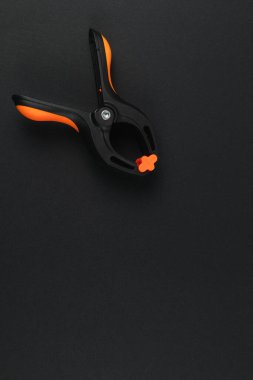 Siyah ve turuncu klempleme aracı karanlık bir yüzeyde duruyor, çeşitli zanaat ve onarım işlerinde kullanılmaya hazır, pratik tasarımı ve işlevselliğini vurguluyor.