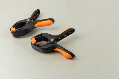 Turuncu kabzalı iki kıskaç pürüzsüz bir yüzeye oturur ve çeşitli el yapımı ve DIY projelerinde kullanılmaya hazırdır. Tasarımları malzemeleri güvenli bir şekilde tutmada yardımcı oluyor..