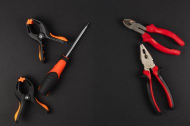 Çeşitli ev onarım projeleri için ideal olan klempler, tornavida ve pense gibi temel araçlar koyu bir arkaplanda görüntülenir.