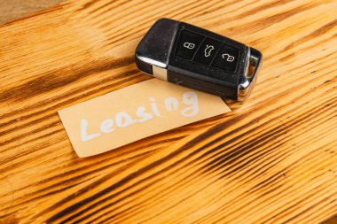 Bir araba anahtarı, üzerinde kira sözleşmesi yazan bir notla birlikte ahşap bir masanın üzerinde duruyor. Bu sahne araba kiralama seçenekleri veya işlemleri üzerine bir odak önerir.