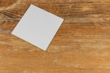 Düz kare bir kağıt parçası, yüzeyin doğal dokusunu gösteren ahşap bir masanın üzerinde duruyor. Yumuşak ışıklandırma sahnenin basitliğini arttırır.