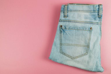 Açık mavi kot pantolon düzgün katlanmış ve yumuşak pembe bir arka plana yaslanmış, günlük kıyafet için mükemmel bir stil sergiliyor..