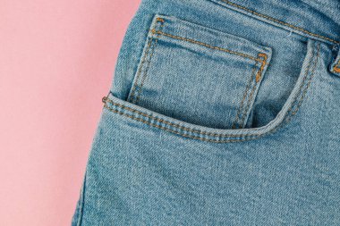 Yakından bakınca turuncu iplikle dikilmiş açık mavi kot pantolonun yumuşak pembe arka planda olduğunu görüyoruz. Basit ve zarif tasarım ayrıntıları göze çarpar.