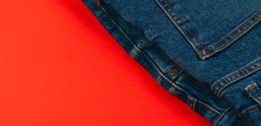 Denim kotları güzelce katlanır ve parlak kırmızı bir arka plana yerleştirilir, çarpıcı bir görsel karşıtlık yaratarak gündelik tarzlarını ön plana çıkarır..