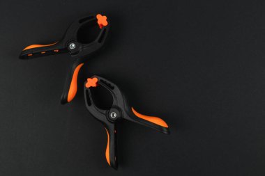 İki siyah ve turuncu klemp koyu bir arka planda, tasarımlarını sergiliyorlar. Bu araçlar çeşitli projeler sırasında ögeleri güvenceye almak için idealdir.