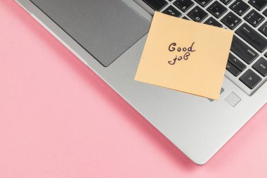 Üzerinde iyi iş yazılı yapışkan bir not, parlak pembe bir arka plana karşı bir dizüstü bilgisayarın klavyesine yerleştirilir, bir çalışma ortamında motivasyonu teşvik eder.