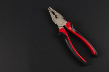 Kırmızı ve siyah kabzalı bir çift kerpeten, çeşitli ev projeleri ve onarım için hazır, dayanıklı alet tasarımı ve işlevi gösteren, karanlık bir yüzeyde oturur..