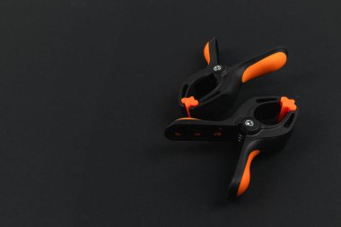 Siyah ve turuncu kıskaçlar karanlık bir masada dinleniyor. Ahşap işçiliği ya da el işi için ideal. Bunun gibi araçlar güvenli materyallere yardımcı olur.