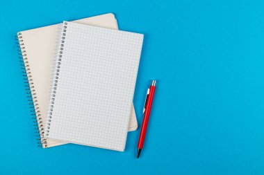 Canlı bir mavi yüzey üzerinde iki boş defter ve bir kırmızı kalem dinlenme, yazma veya çizim projeleri için fikirler ve yaratıcılığa davet.