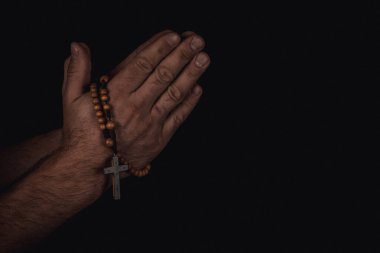 Elleri dua ederken birbirine kenetlenir, bir tespih tutar, karanlık bir arka plana yaslanır, barışçıl ve yansıtıcı bir atmosfer yaratır..