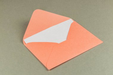 Açık turuncu bir zarf gri bir yüzeyde duruyor, beyaz iç kapağını gösteriyor. Olay yeri, mektup veya kart gönderme hazırlığı öneriyor..