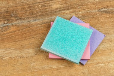 Farklı renklerde üç sünger ahşap bir masaya güzelce istiflenmiş. Aydınlık ve davetkar bir ortam. Temizlik işleri, sanat ve el sanatları için mükemmel..