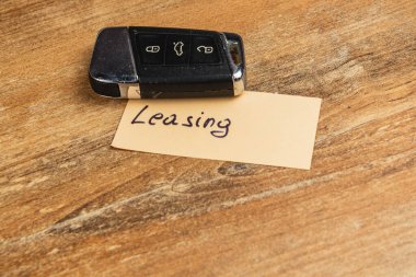 Bir anahtarlık kira kontratı yazan bir kağıt parçasının üzerinde duruyor. Ayar doğal bir ahşap yüzeye sahip, bu da gündelik veya iş bağlamına işaret ediyor..