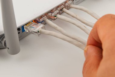 Evde bir el ağ kablolarını yönlendiriciye bağlıyor. Bu ayar, çeşitli aygıtlar için istikrarlı bir internet bağlantısı kurmak için gereklidir.