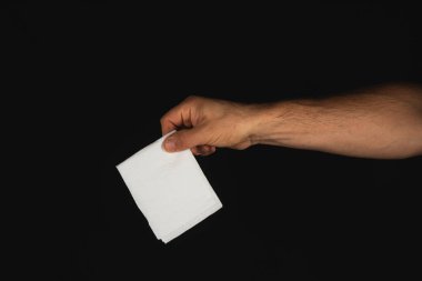 Bir el, beyaz bir peçeteyi sıkıca kavrar, koyu bir arka plana şiddetle zıt düşer, basit ama çarpıcı bir anı yakalar..